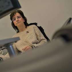 Eine nachdenkliche Frau sitzt an einem Schreibtisch, umgeben von Bürogeräten, und scheint sich auf ihre Aufgaben zu konzentrieren.