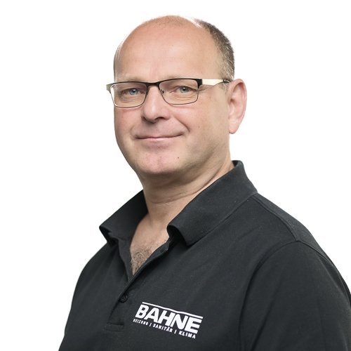 Ein Mann mit Brille und einem schwarzen Polohemd mit dem Logo 'BAHNE' lächelt freundlich in die Kamera.