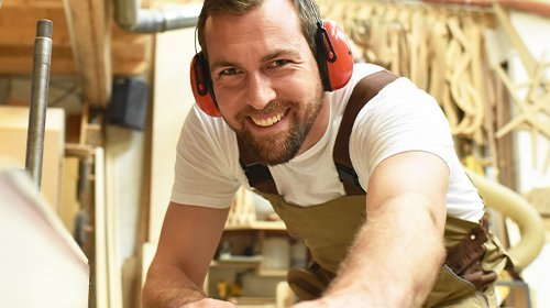 Ein Tischler mit Gehörschutz hält ein Holzbrett