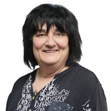 Eine lächelnde Frau mit schwarzem, schulterlangem Haar trägt ein schwarzes Oberteil mit weißen Schriftzügen.