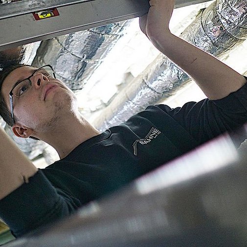 Ein Anlagenmechaniker der eine Wasserwaage an einem vierkant Rohr hält