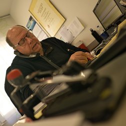 Der Mann am Schreibtisch telefoniert und notiert wichtige Informationen, umgeben von Büromaterialien und einem Computer.